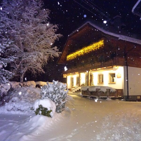 The exterior of the Farm House at night, covered in snow with decorative lights and falling snowflakes. The exterior of the Farm House at night, covered in snow with decorative lights and falling snowflakes.