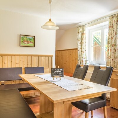 Dining area of the Ferienwohnung with a wooden table, corner bench, chairs, and a television.