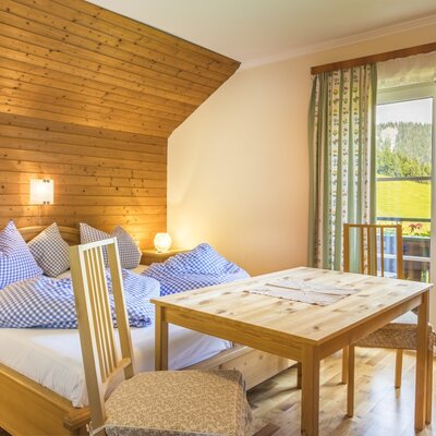 Bedroom in the Ferienwohnung with a double bed, wooden walls, a dining table, and balcony access with mountain views.