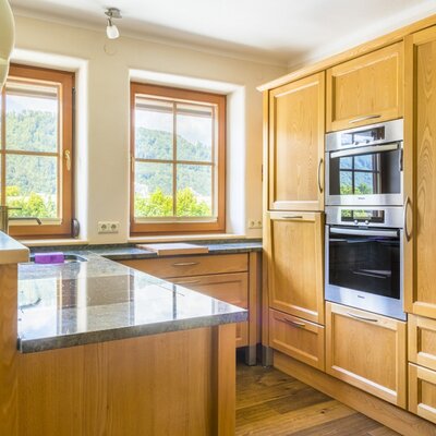 Farm House kitchen equipped with wooden cabinets, built-in oven and microwave, granite countertops, an island with a sink and breakfast bar, and mountain views from the windows.