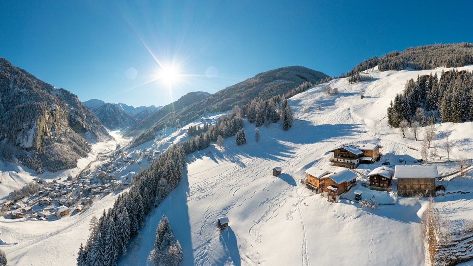The farmhouse in a snow-covered winter landscape with a view of the valley and the surrounding mountains.