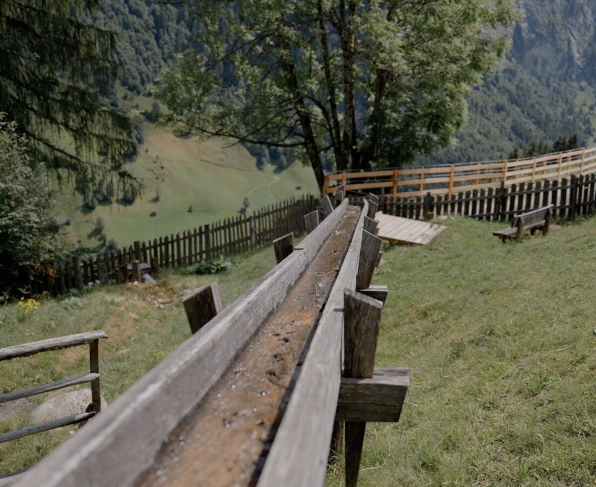 Wooden water channel at the farmhouse, offering mountain views and a green meadow.