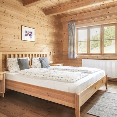 Double bedroom in the farmhouse with a wooden bed, wood-paneled walls, and a window offering a view of nature.