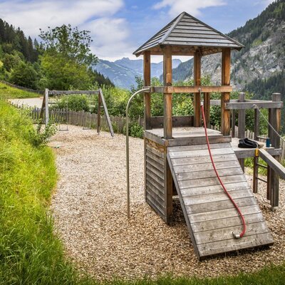 The farmhouse's inviting children's playground featuring wooden play equipment against a scenic mountain backdrop.