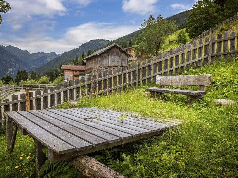 The farmhouse's inviting outdoor area featuring a rustic wooden bench and scenic views of the surrounding mountain landscape.