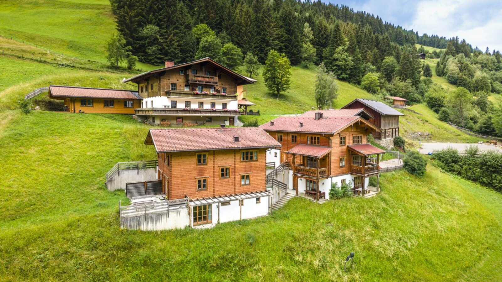 The inviting farmhouse is nestled among lush green meadows and forested mountain slopes.