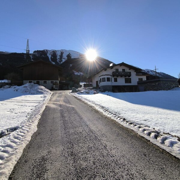 The Farm House and its entrance road in winter, surrounded by snow-covered fields and sunlit mountains.