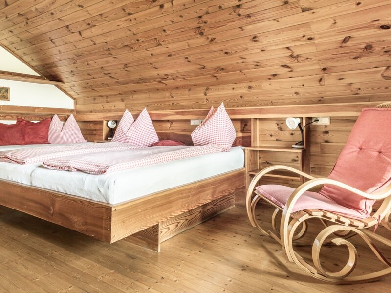 Bedroom in the farmhouse with a double bed, wooden furnishings, and a rocking chair.