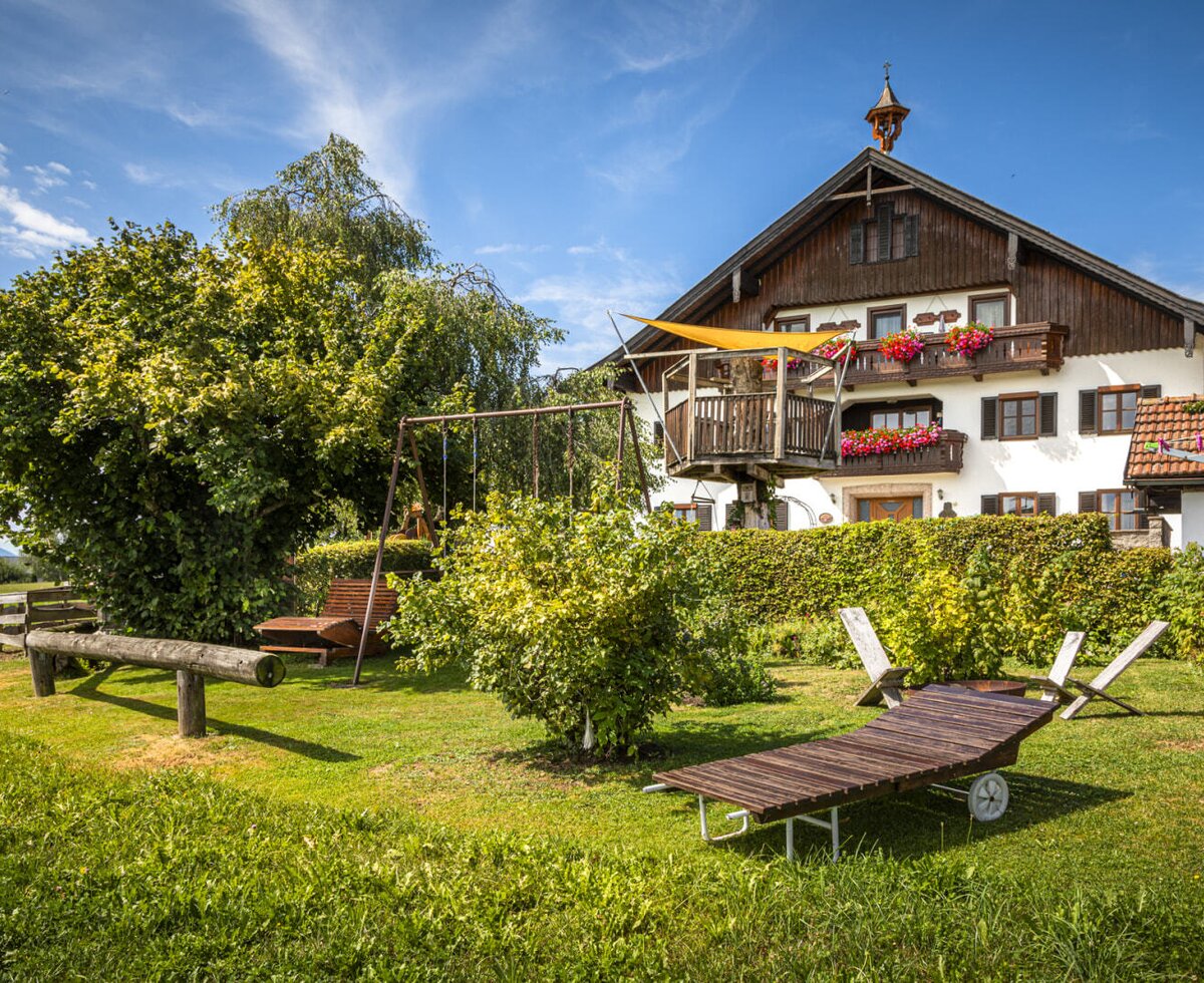 The farmhouse's inviting garden, featuring a spacious lawn, comfortable sun loungers, and a children's play area set against the traditional main building.