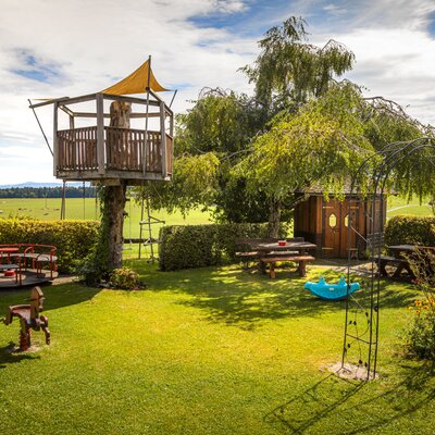 The farmhouse's inviting garden features a children's playground with a wooden treehouse, play equipment, and cozy outdoor seating areas.