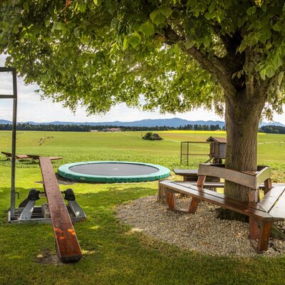 The farmhouse's inviting play area, featuring a trampoline, a seesaw, and a shaded bench with scenic mountain views.