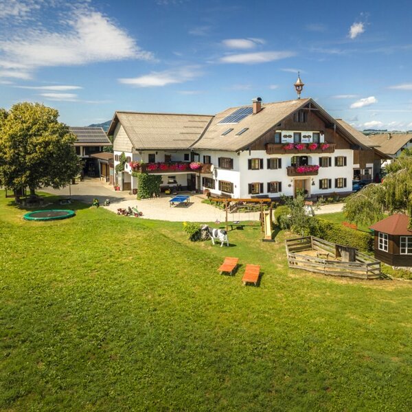 The inviting farmhouse featuring a spacious green lawn, a trampoline, and outdoor play areas for children.
