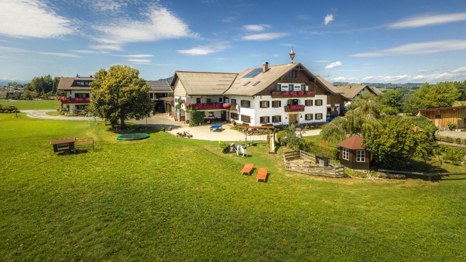 The inviting farmhouse featuring a spacious green lawn, a trampoline, and outdoor play areas for children.