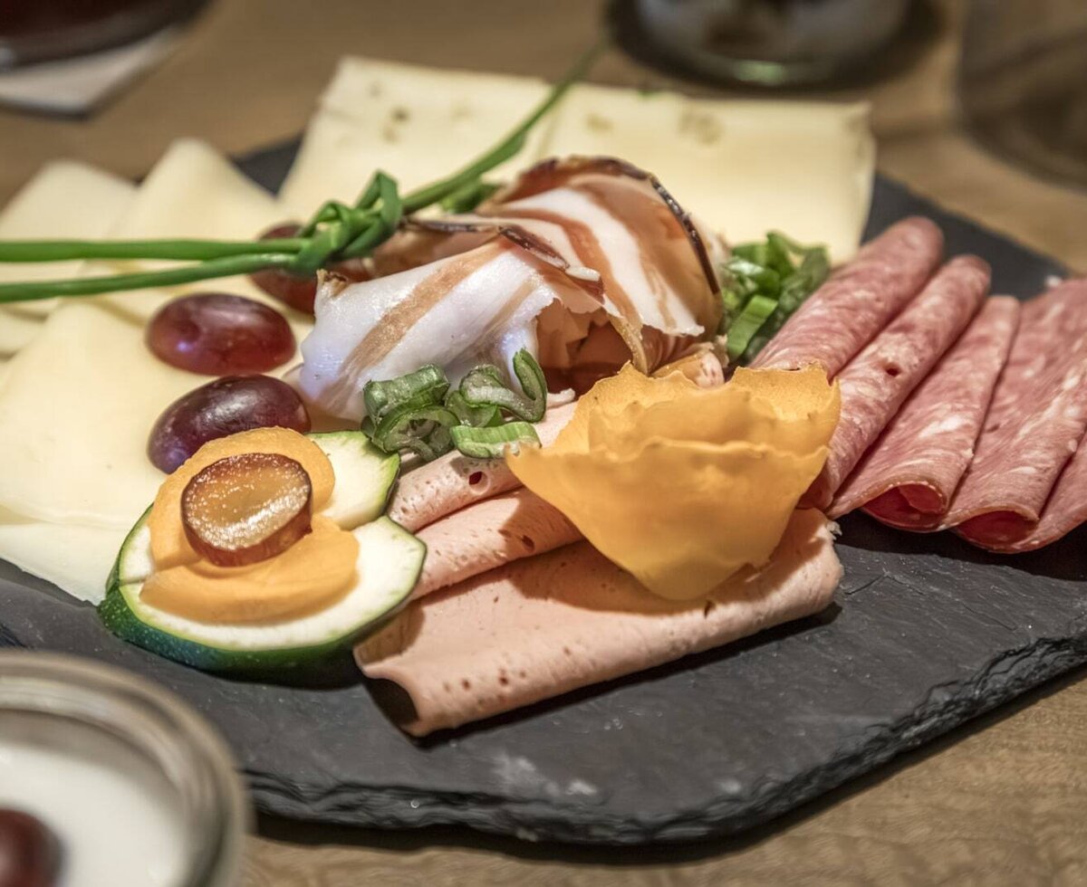 A platter with cold cuts, cheese, grapes, and vegetables, part of the rich farmhouse breakfast at the Bauernhof.