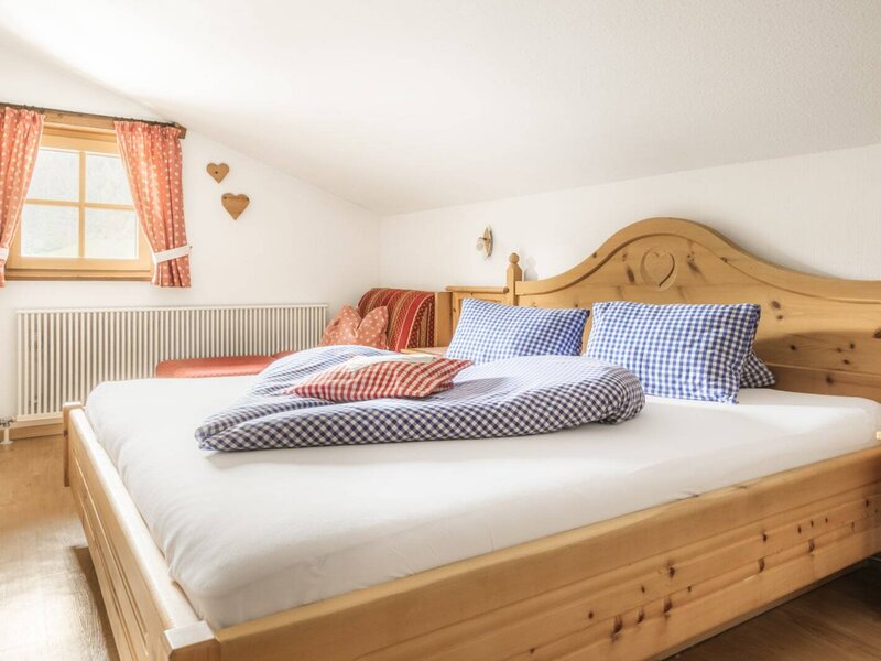 Bedroom in the farmhouse with a double bed, checkered bedding, wooden furniture, and a seating area under the window.