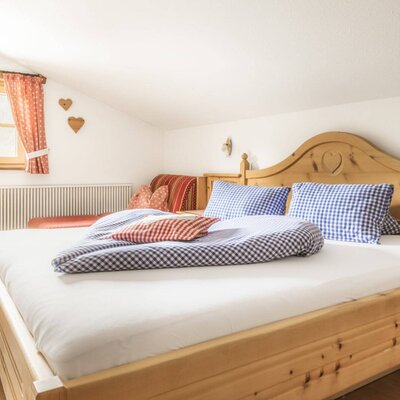 Bedroom in the farmhouse with a double bed, checkered bedding, wooden furniture, and a seating area under the window.