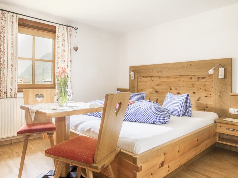 Double bedroom in the farmhouse with a wooden bed, nightstand, table and chairs, and a window with mountain views.