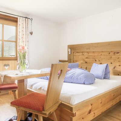 Double bedroom in the farmhouse with a wooden bed, nightstand, table and chairs, and a window with mountain views.
