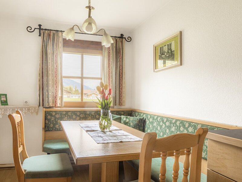 Dining area in the holiday apartment of the farmhouse, featuring a wooden table, corner bench, and a window view of the countryside.