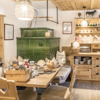 The farmhouse parlor of the Bauernhof, set up for the rich farmhouse breakfast with a green tiled stove and wooden furniture.
