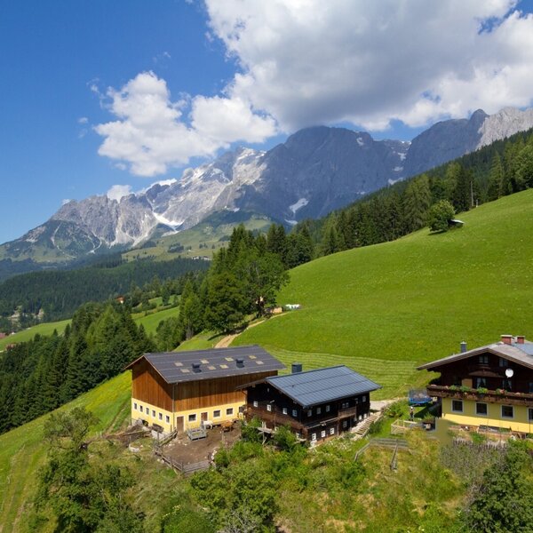 The Farm House is situated on a green hillside with a mountainous backdrop.