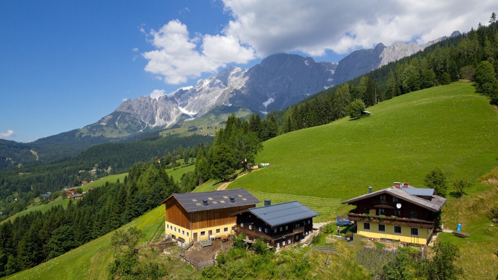 The Farm House is situated on a green hillside with a mountainous backdrop.