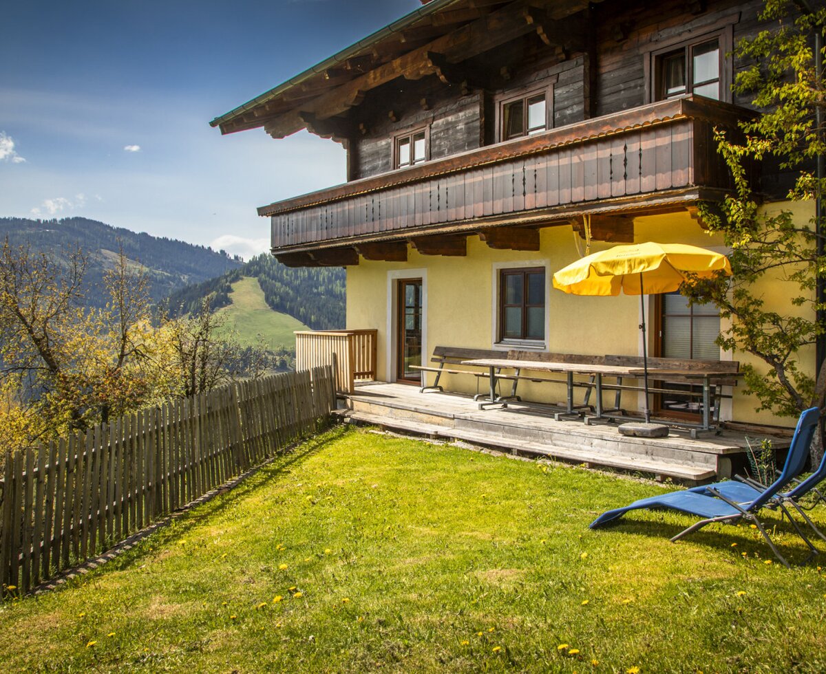 The farm house offers an outdoor terrace with a dining set and sun umbrella, a grassy garden with lounge chairs, and views of the mountains.
