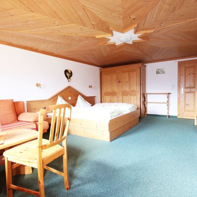 Ferienwohnung sleeping and living area with a double bed, sofa, coffee table, wooden furniture, and a wooden ceiling.