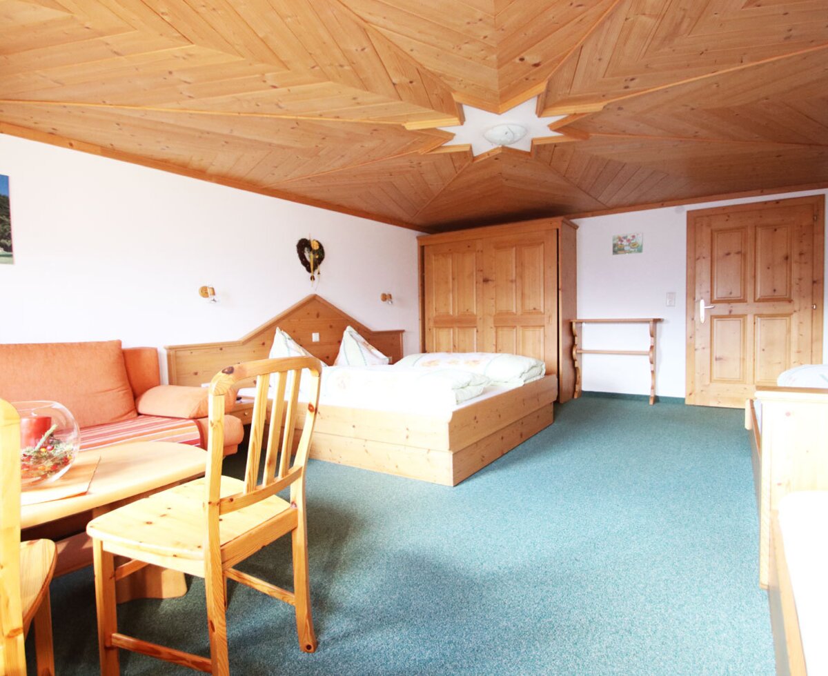 Ferienwohnung sleeping and living area with a double bed, sofa, coffee table, wooden furniture, and a wooden ceiling.