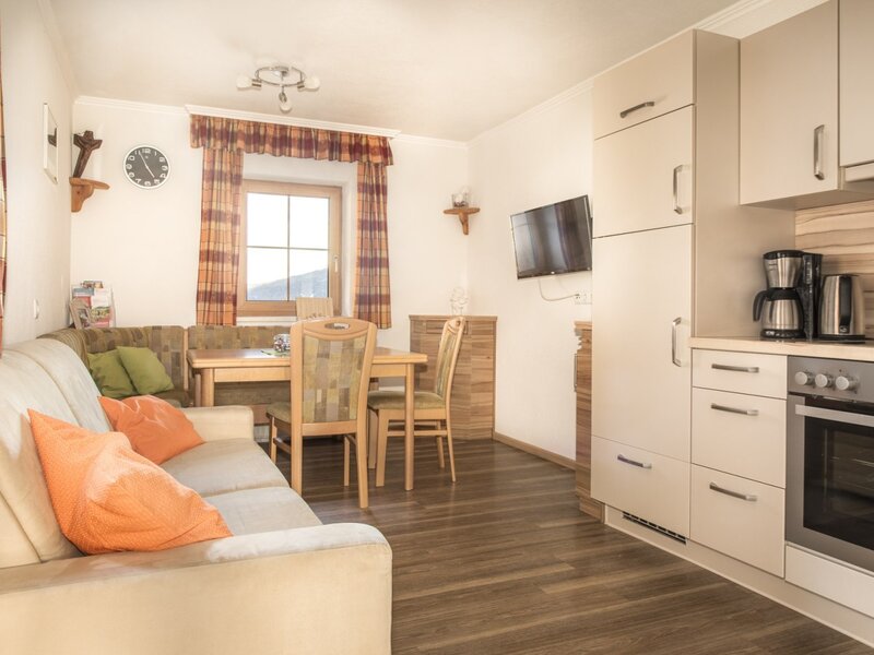 Living and dining area of the holiday apartment featuring a sofa, dining table, corner bench, TV, and an integrated kitchenette with an oven and coffee machine.