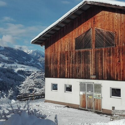 A farm building at the Farm House, featuring wooden siding and a white lower section, surrounded by snow and a mountain landscape.