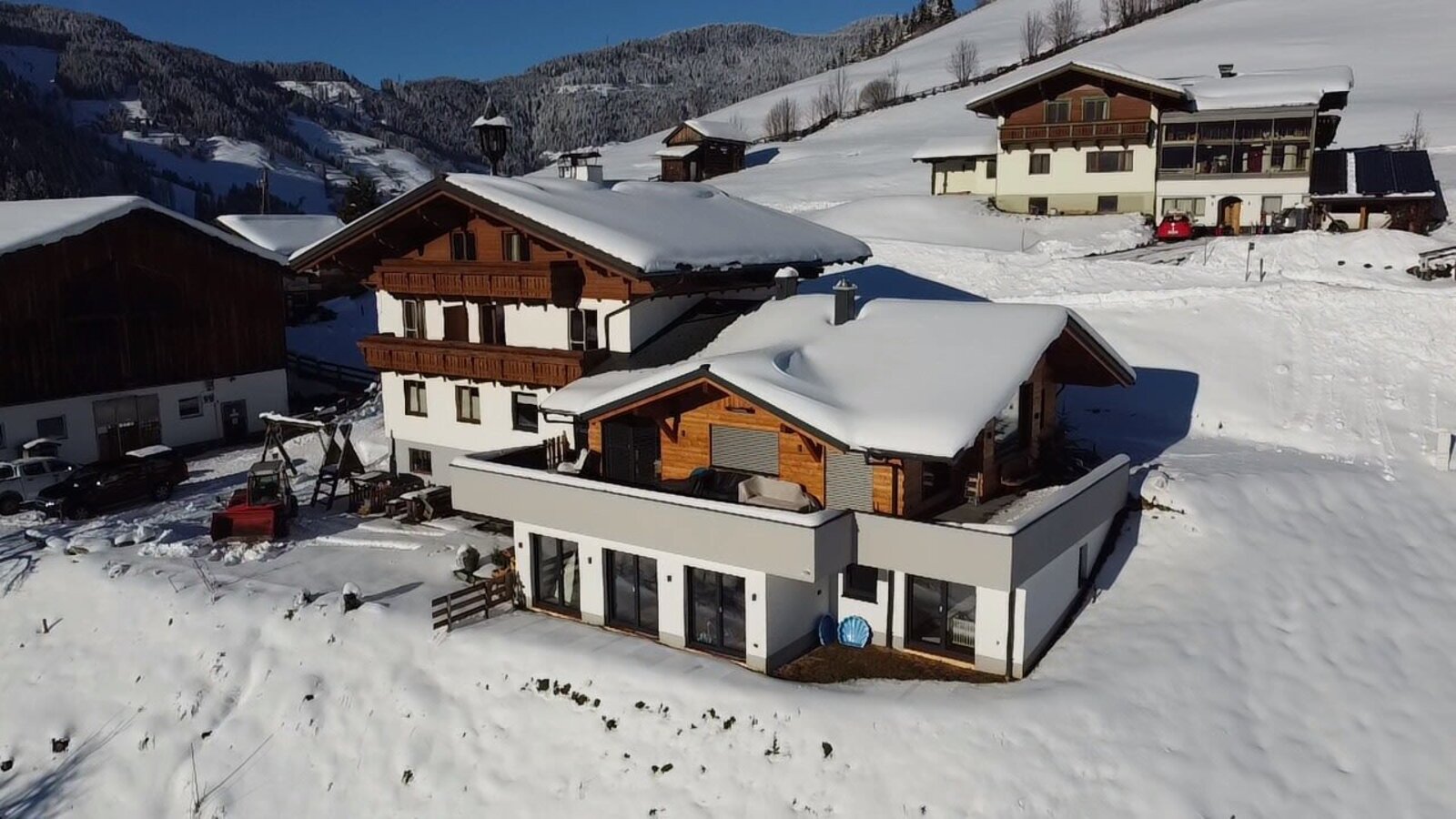 The snow-covered Farm House exterior, featuring both traditional architecture and a modern extension, set against a winter mountain landscape.