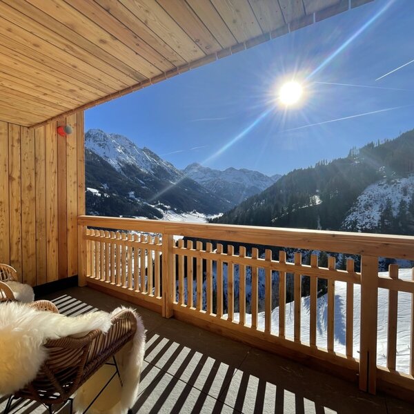 Balcony of a holiday flat at the Farm House, with seating and a sunny view of the snow-covered mountains.