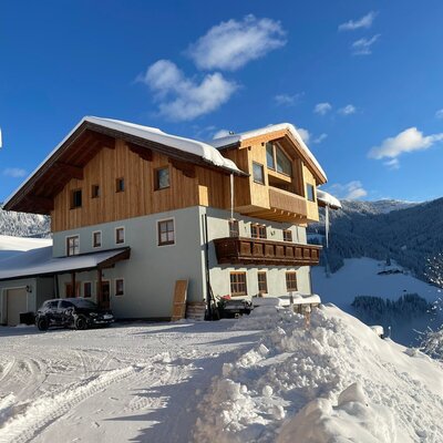 The exterior of the Farm House in winter, featuring snow-covered roofs and a mountain panorama.