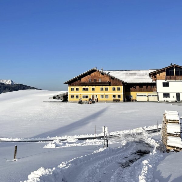 The Farm House, featuring a yellow and white facade with traditional wooden elements, stands amidst a snowy landscape with distant mountains under a clear blue sky. The Farm House, featuring a yellow and white facade with traditional wooden elements, stands amidst a snowy landscape with distant mountains under a clear blue sky.