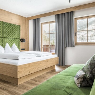 Double bedroom in the farmhouse with solid wood furnishings, green headboard, sofa, and mountain view.