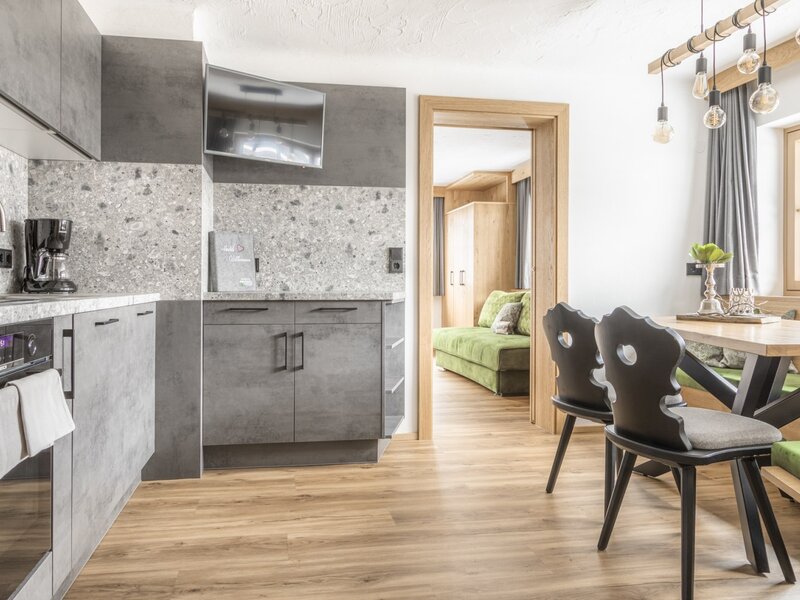 Kitchenette with flatscreen and dining area with wooden table and bench in the farmhouse, with access to another room.