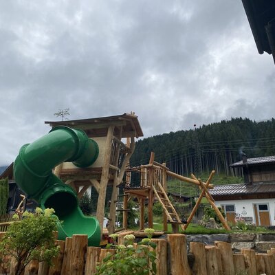 Farmhouse playground with a wooden play tower, slide, and swing.