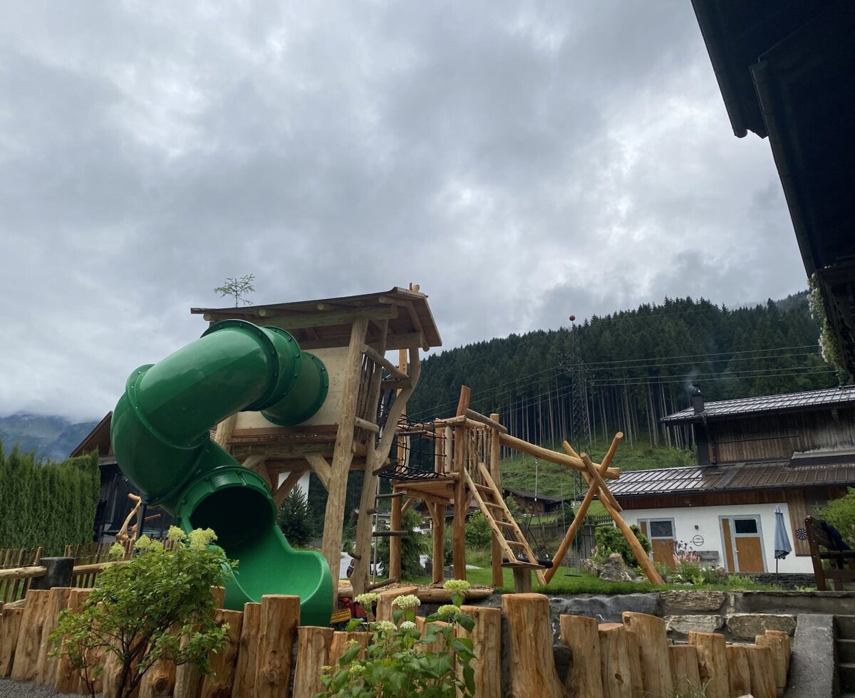 Farmhouse playground with a wooden play tower, slide, and swing.