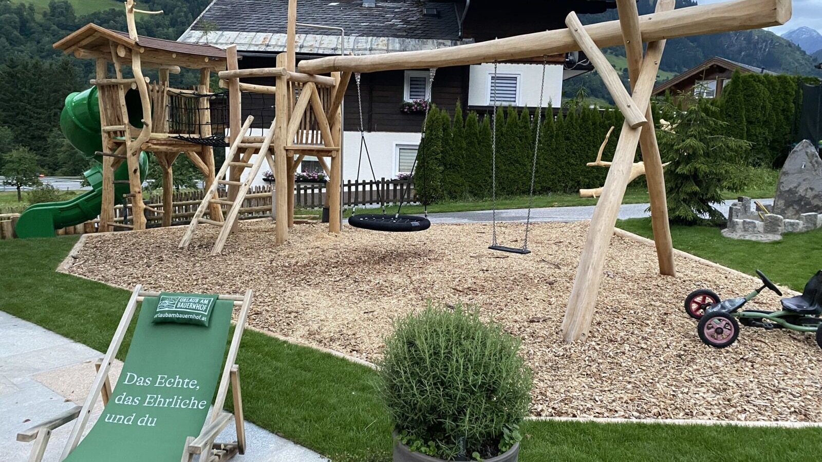 The Bauernhof's playground, featuring a wooden tower, slide, and swings on a wood chip surface.