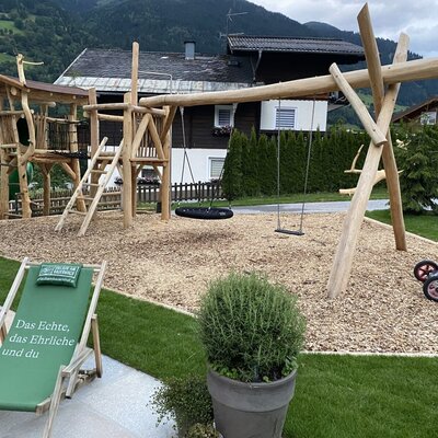 The Bauernhof's playground, featuring a wooden tower, slide, and swings on a wood chip surface.