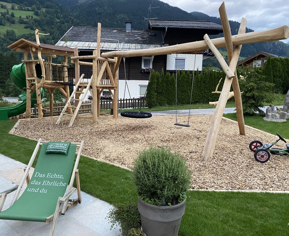 The Bauernhof's playground, featuring a wooden tower, slide, and swings on a wood chip surface.