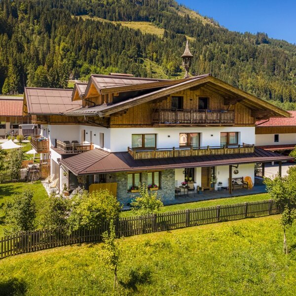 The inviting farmhouse is situated amidst a lush green meadow with scenic views of the surrounding mountains.