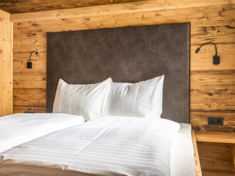 Bedroom in the Farm House featuring a bed with white linen, a dark headboard, wooden wall paneling, and wall-mounted reading lights.
