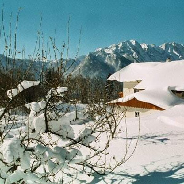 The Farm House exterior in winter, with its snow-covered roof and surrounding grounds, set against a backdrop of mountains.