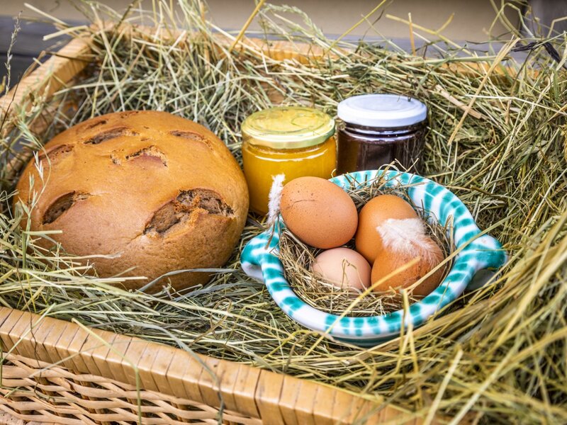 Fresh bread, eggs in a dish, and jars of preserves arranged in a hay-filled basket at the Farm House.
