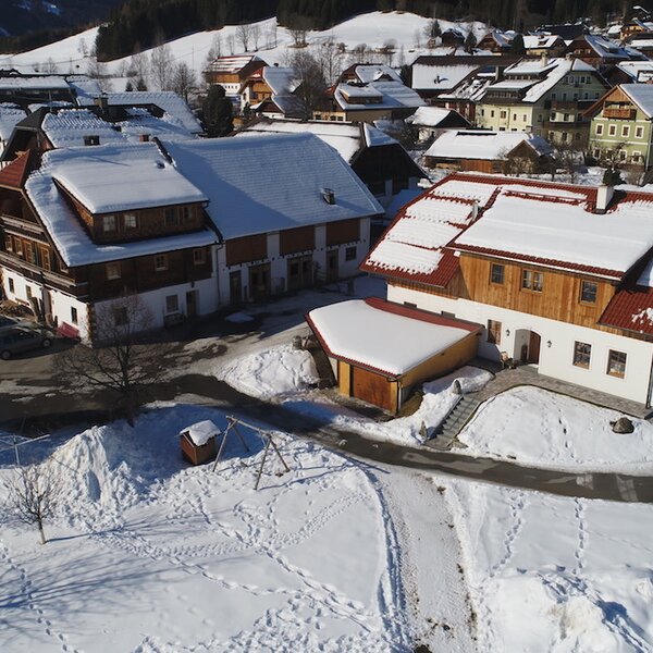 The traditional farm house buildings, with snow-covered roofs, are situated in a winter village landscape, featuring outdoor play equipment on the grounds. The traditional farm house buildings, with snow-covered roofs, are situated in a winter village landscape, featuring outdoor play equipment on the grounds.