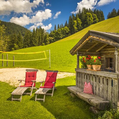 The Farm House offers a beach volleyball court and sun loungers for guest recreation, set against a green hillside with a small wooden hut.