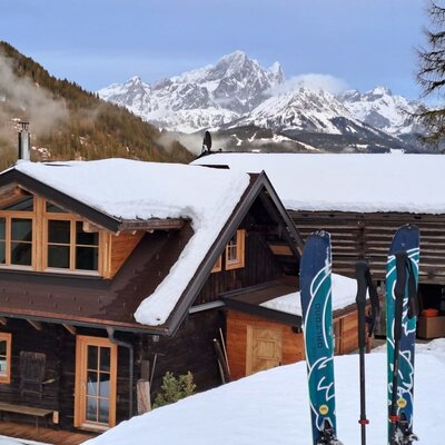 The farmhouse in winter, featuring a snow-covered roof, mountain views, and skis in the foreground.