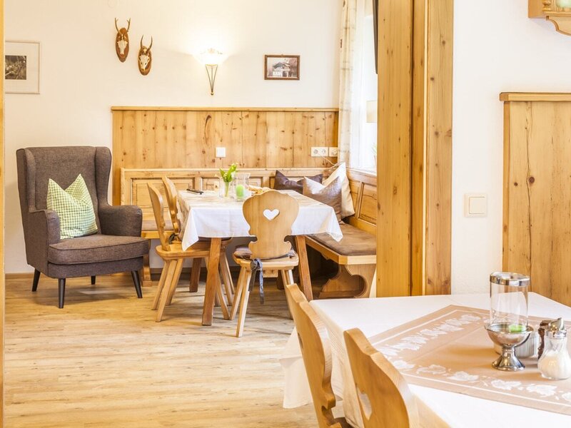 The lounge area of the Farm House features a dining table with a wooden bench and chairs, alongside an armchair, all with traditional solid wood elements.